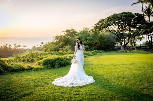 Bride in elegant white wedding dress standing on Hawaii golf course at golden hour sunset