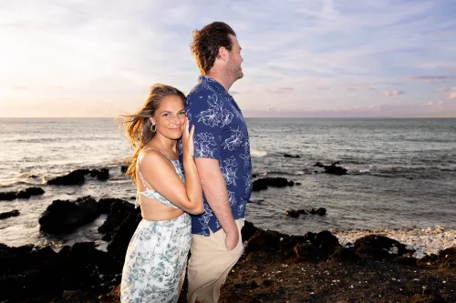 Bride and groom on volcanic black lava rocks by ocean at dusk in Hawaii
