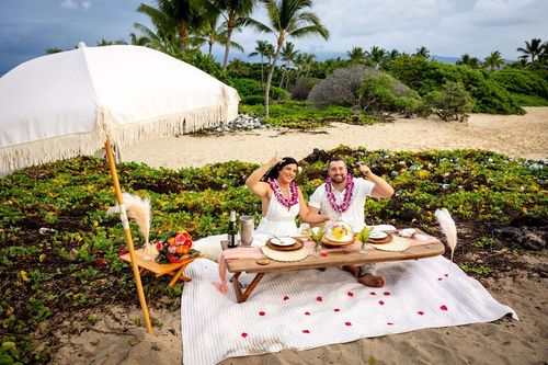 Luxury beach picnic with white blanket, cushions, tropical flowers, and ocean view in Hawaii