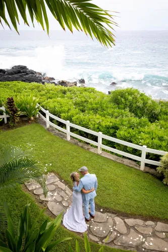 Bride in white dress on lush green hillside with white fence in Hawaii