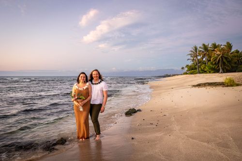 Newlyweds walking hand in hand on secluded tropical beach with palm trees in Hawaii
