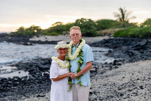 Newlywed couple standing on black lava rock beach with tropical leis in Hawaii