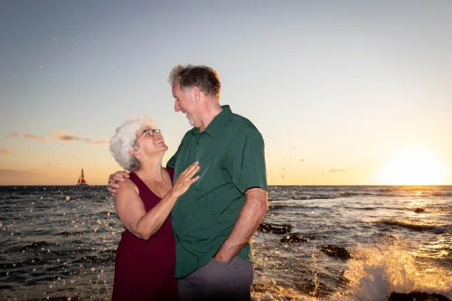Couple embracing on sandy Hawaii beach during romantic golden hour sunset
