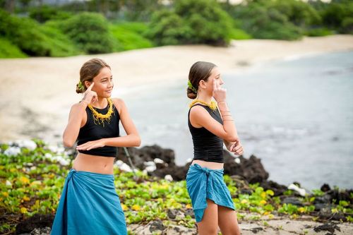 Girls blue skirts dancing on lush green tropical hillside in Hawaii
