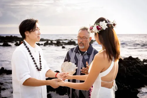 Wedding officiant performing traditional Hawaiian ceremony for couple on volcanic lava rocks by ocean