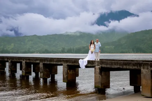 Newlywed couple on a bridge overlooking misty green mountains in Hawaii