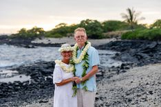 Newlywed couple standing on black lava rock beach with tropical leis in Hawaii